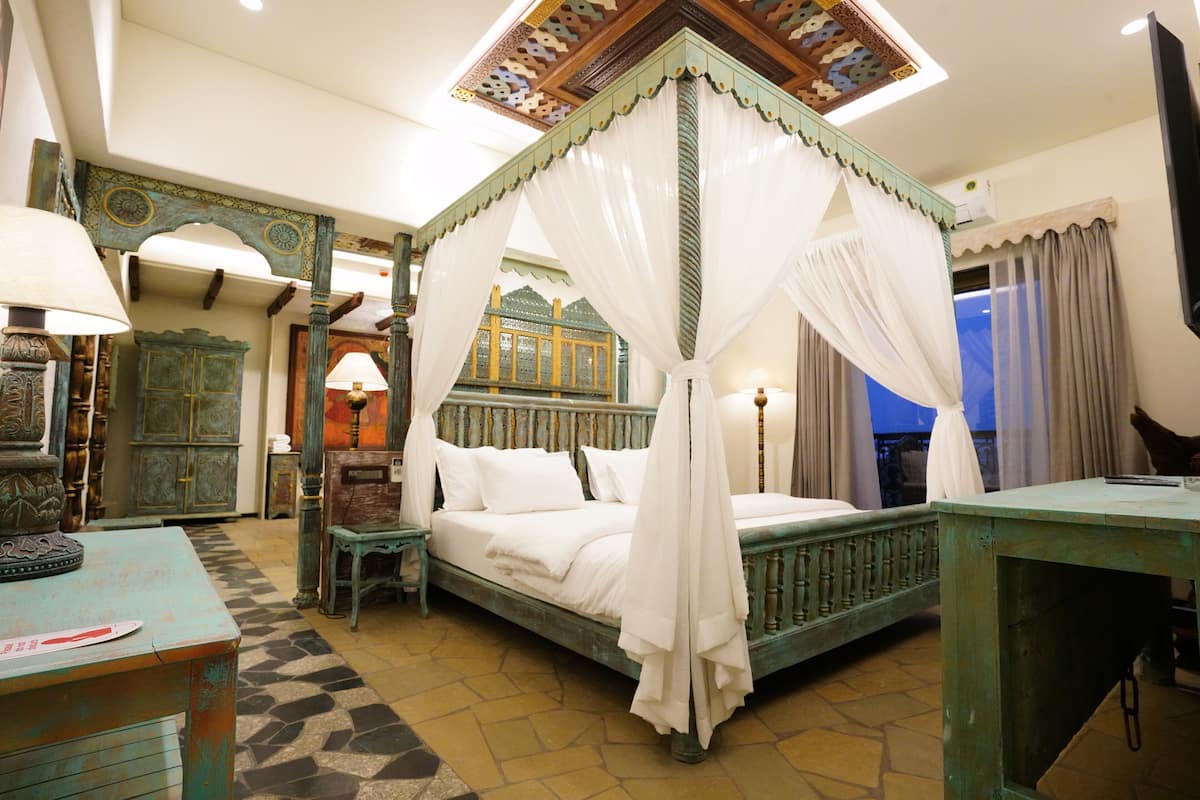 A four-poster canopy bed with white linens, a wooden nightstand, a small table with a lamp, and a checkered floor.