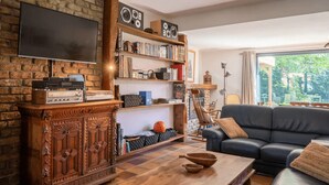 Un salón con pared de ladrillo, un mueble de madera, un sofá de cuero negro y una estantería llena de libros y objetos decorativos.