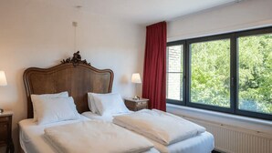 Una cama doble con ropa blanca, un cabecero de madera, dos mesitas de noche con lámparas y una ventana con cortina roja.
