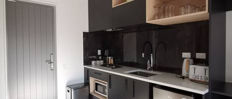 A modern kitchen with a built-in oven, microwave, and dishwasher. There is a sink with a faucet, a stove, and a toaster. The kitchen has black cabinets and a white countertop.