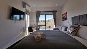 Habitación de hotel moderna con una cama grande, un televisor de pantalla plana, un escritorio y vistas a un paisaje montañoso por la ventana.