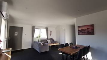 Ein modernes Wohnzimmer mit grauem Sofa, einem Holzespeisetisch mit Stühlen, einem kleinen Couchtisch und einem Gemälde an der Wand.