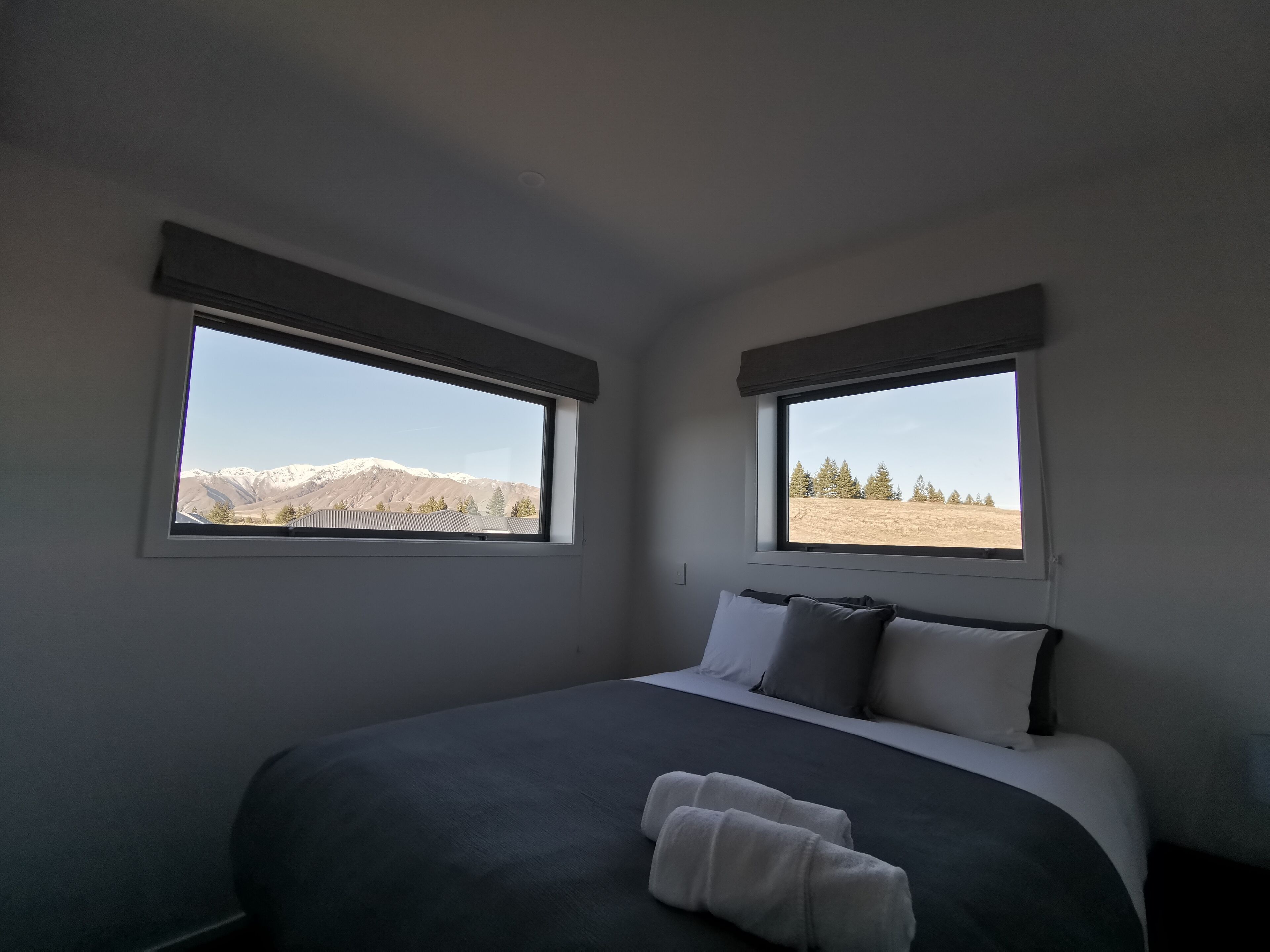 A bedroom with two windows, a bed with gray bedding, and a view of mountains.