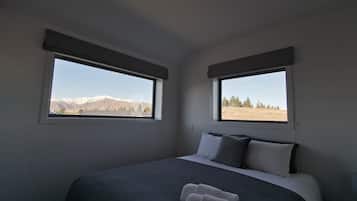 A bedroom with two windows, a bed with gray bedding, and a view of mountains.