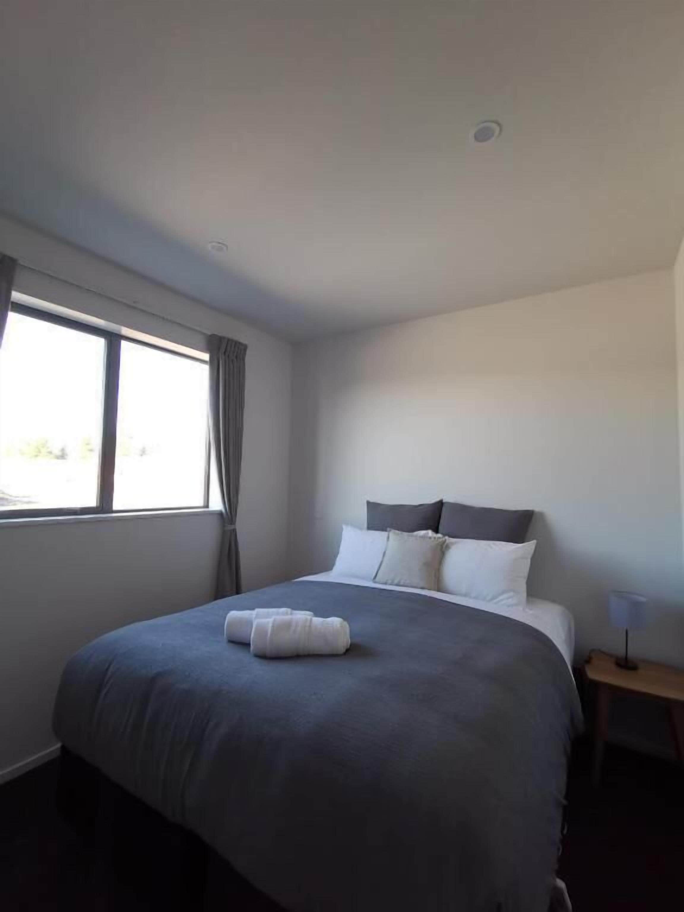 A modern hotel room with a large bed, a bedside table, and a window with curtains.