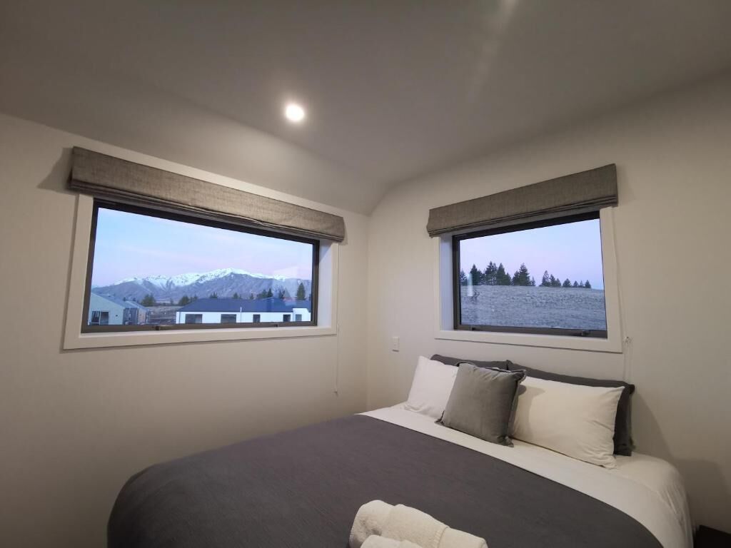 Un dormitorio con una cama grande, dos ventanas con vistas a la montaña y una lámpara de techo.
