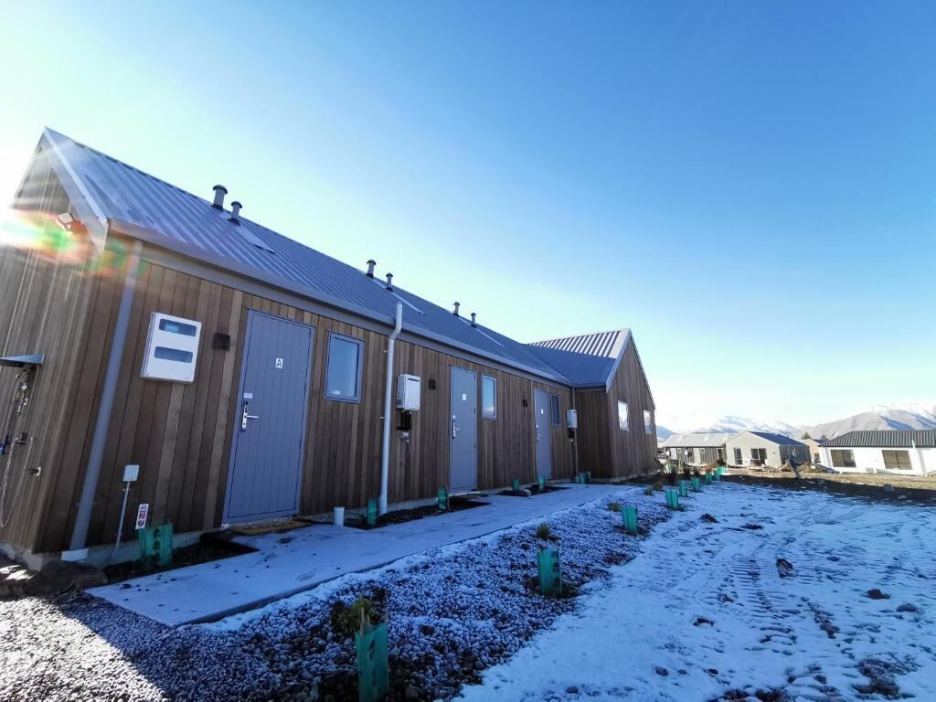 A long, wooden building with multiple doors and windows, set against a snowy landscape with mountains in the background.