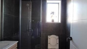 A compact bathroom with a glass-enclosed shower, a toilet, and a window providing natural light.