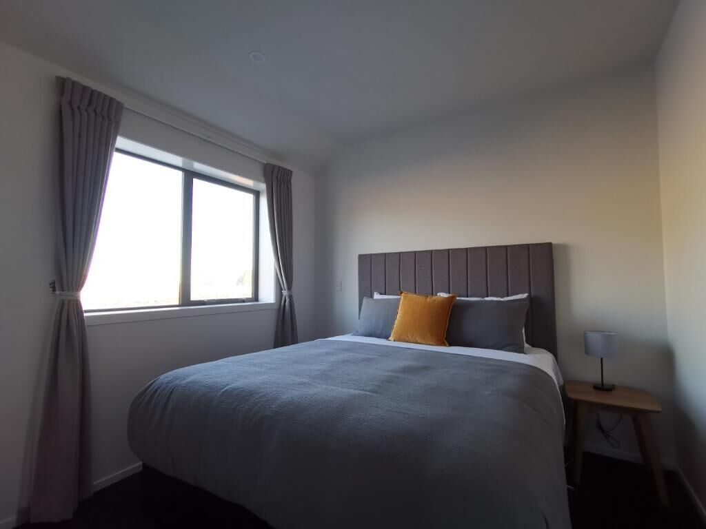 A modern hotel room with a large bed, a bedside table, and a window with curtains.