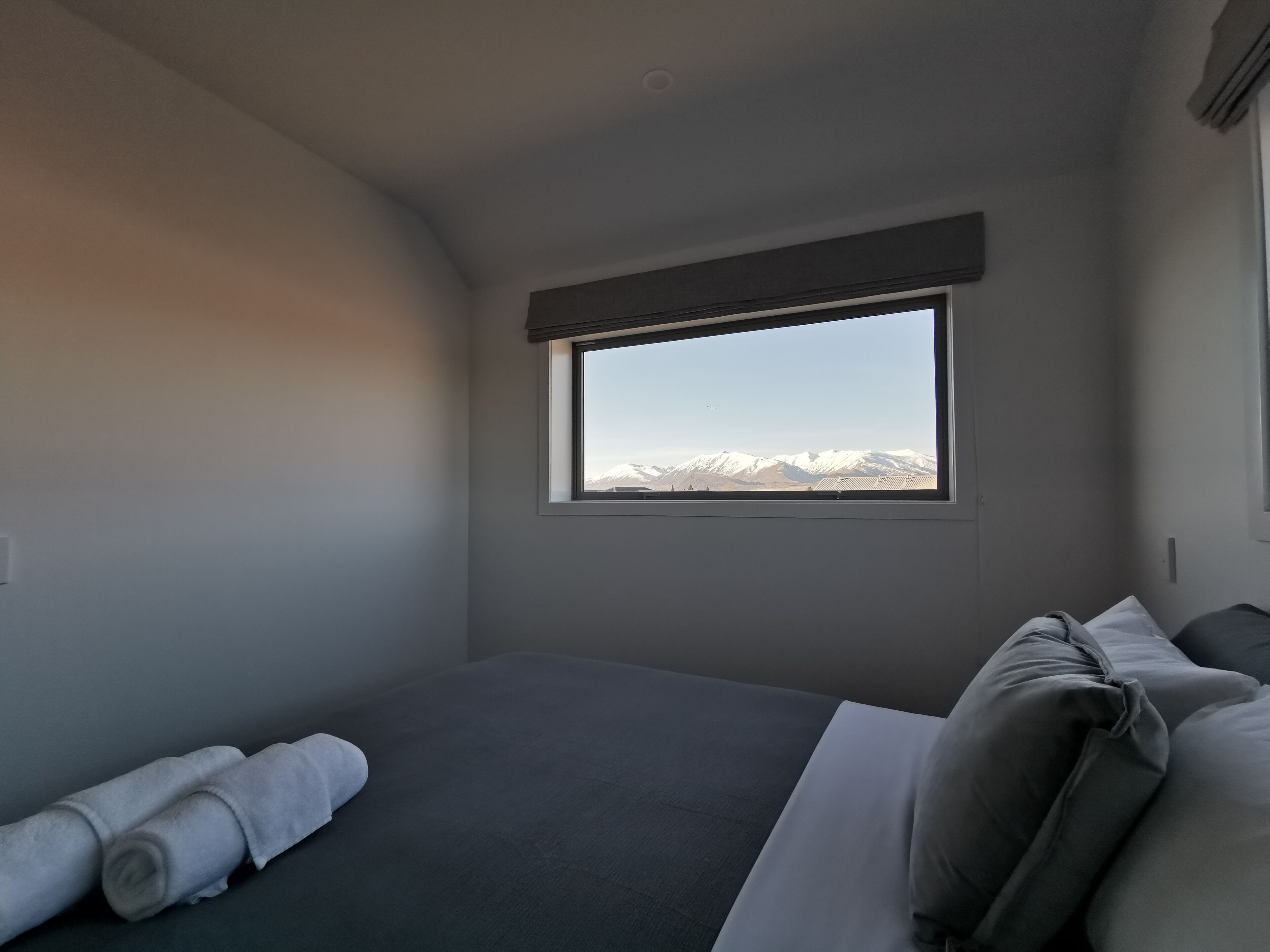 A bedroom with a bed, a window with a mountain view, and a rolled towel on the bed.