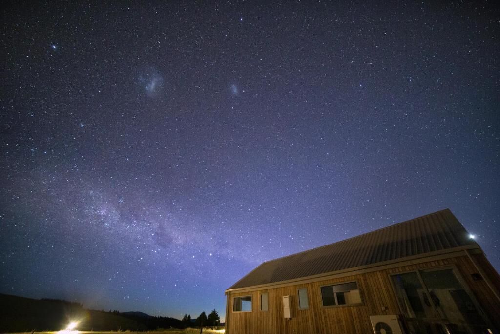 A wooden cabin under a starry night sky with a visible Milky Way.