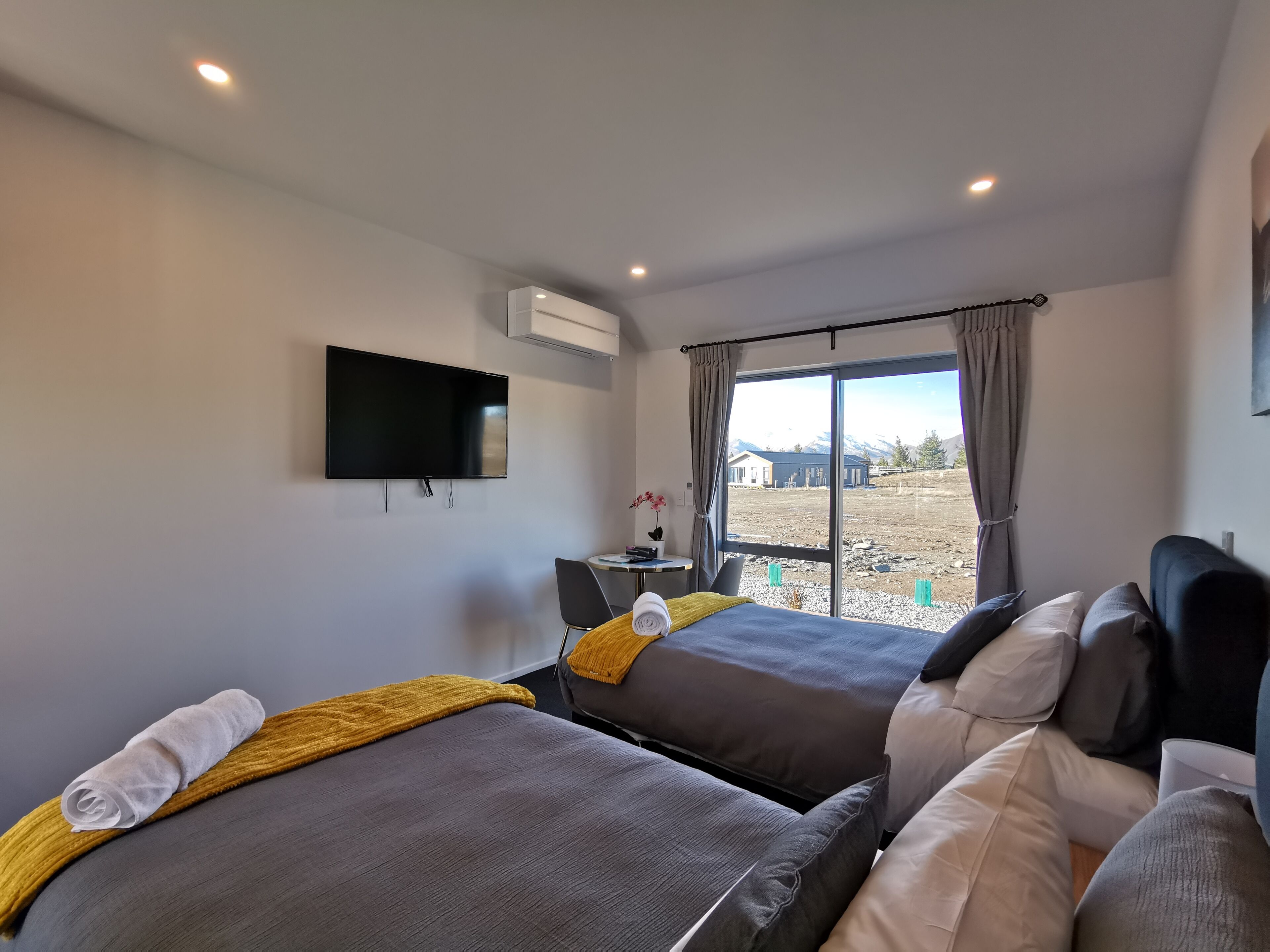 A modern hotel room with two beds, a flat-screen TV, and a large window with a view of mountains.
