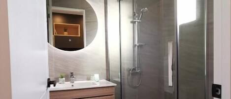 A modern bathroom with a glass-enclosed shower, a round mirror, and a wooden vanity.