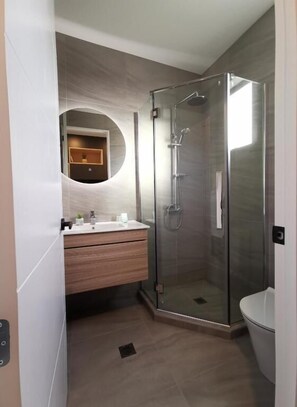 A modern bathroom with a glass-enclosed shower, a round mirror, and a wooden vanity. - Skyrim Lodge (Lake Tekapo)