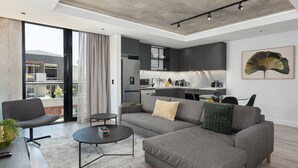 A modern living room with a grey sectional sofa, a coffee table, and a dining area. - The Signature 414 (Cape Town)