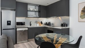 A modern kitchen with a built-in dishwasher, microwave, and coffee maker. There is a glass dining table with black chairs. - The Signature 414 (Cape Town)