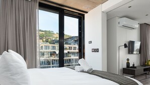 A modern hotel room with a large bed, a desk, and a view of buildings through a sliding door. - The Signature 414 (Cape Town)
