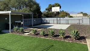 En lukket baghave med en overdækket terrasse, en basketballkurv og et lille haveområde med planter.