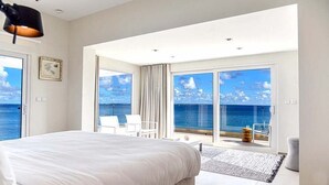 Une chambre dotée d’un grand lit, offrant une vue sur la mer grâce à de larges baies vitrées et comprenant un balcon aménagé avec des sièges.