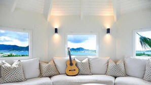 Un canapé blanc avec des coussins à motifs, une guitare et une table sur laquelle se trouvent un livre et un magazine.