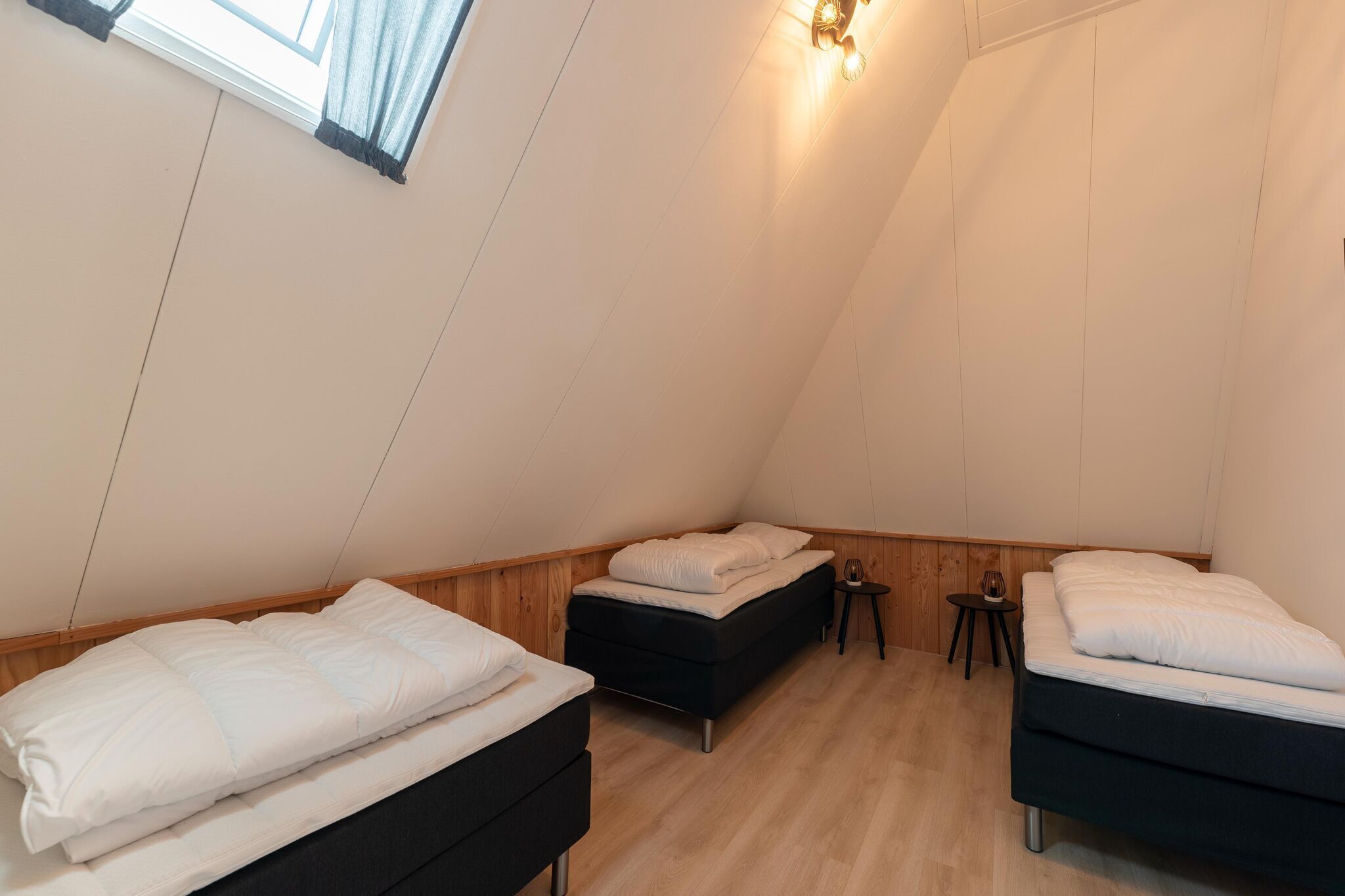 A triangular room with two beds, a small table, and a wall-mounted light fixture.