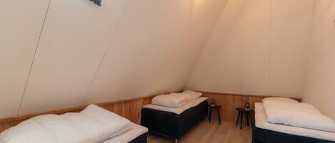 A triangular room with two beds, a small table, and a wall-mounted light fixture.
