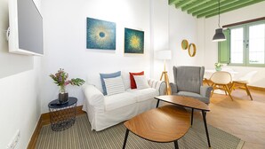 A modern living room with a white sofa, a black and white checkered chair, a round wooden coffee table, and two abstract paintings on the wall. - Cantabria. 1-bedroom in the centre (Sevilla)