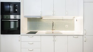 A modern kitchen with white cabinets, a black microwave, a stainless steel oven, a sink with a faucet, and a backsplash. - Cantabria. 1-bedroom in the centre (Sevilla)