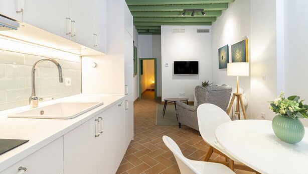 A modern kitchen with white cabinets, a stainless steel sink, and a dining area with a table and chairs. - Cantabria. 1-bedroom in the centre (Sevilla)