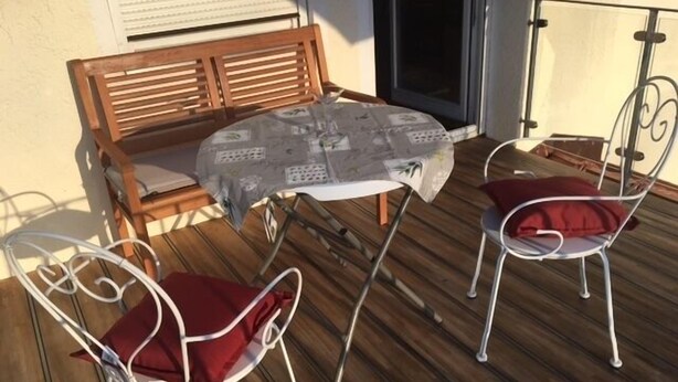 A wooden bench and two white metal chairs with red cushions on a wooden deck. - Apartment with 1 sep. Bedroom, southwest-facing roof terrace, 58 sqm (Prien am Chiemsee)