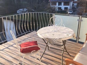 A balcony with a table and chairs, overlooking a body of water and houses.