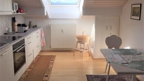 A compact kitchen with a skylight, wooden flooring, and a dining area with a table and chairs. - Apartment with 1 sep. Bedroom, southwest-facing roof terrace, 58 sqm (Prien am Chiemsee)