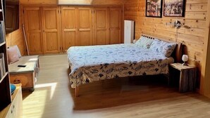 A wooden cabin bedroom with a skylight, a bed with floral bedding, a bedside table, and a nightstand. - Apartment with 1 sep. Bedroom, southwest-facing roof terrace, 58 sqm (Prien am Chiemsee)