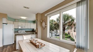 A kitchen with white cabinets, a wooden table with a tray of baked goods, and a view of palm trees through a large window. - Sailmaker 612 - Hosted By Moore AI Rentals (Fernandina Beach)