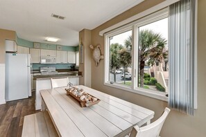 A kitchen with white cabinets, a wooden table with a tray of baked goods, and a view of palm trees through a large window.
