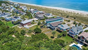 Vue aérienne d’une zone résidentielle côtière, avec des maisons, une plage et un ciel bleu dégagé.