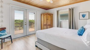 Une chambre avec un lit, un ventilateur de plafond, une armoire en bois et une vue sur un espace extérieur, accessible par une porte vitrée.