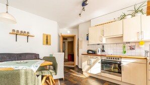 A compact kitchen with a stove, oven, and a dining area with a table and chairs. - Apartment in Ramsau near Ski Slopes (Ramsau)