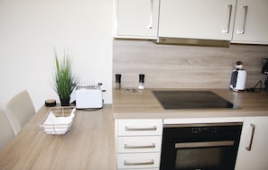 A kitchen with white cabinets, a toaster, a kettle, and a dish rack. - Angel (Binz)
