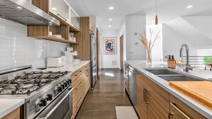 A modern kitchen with a gas stove, stainless steel appliances, wooden cabinets, and a large island with a sink. - 4313 Fremont · 3b2.5b Fremont Gem w/ Seattle Skyline & Lake View (Seattle)