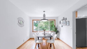 A modern dining room with a large window, a chandelier, and a refrigerator in the background.