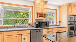 A modern kitchen with wooden cabinets, stainless steel appliances, and a window with a view of greenery.
