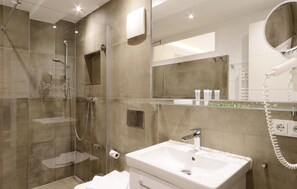 Ein modernes Badezimmer mit einer Glaskabine zur Dusche, einem weißen Waschbecken und einem Spiegel darüber.