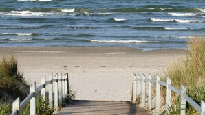 A wooden pathway leading to a sandy beach with waves in the background. - Penthouse Eden (Binz)