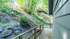 Una escalera de madera que lleva a un espacio cubierto con vistas a un jardín y un edificio.