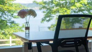 Une table ornée d’un vase de fleurs et une chaise, avec vue sur une étendue d’eau et une végétation luxuriante.