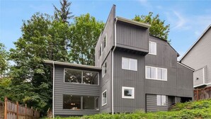 Une maison moderne à deux étages, dotée de fondations en pierre, de grandes fenêtres et d’un toit en pente.
