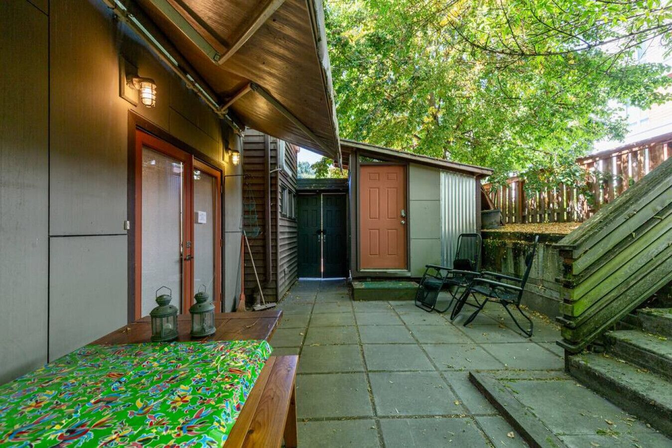 Un espace extérieur abrité, doté d’un banc en bois, d’une petite table et d’une porte donnant accès à un bâtiment.