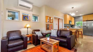 A modern living room with leather sofas, a coffee table, and a dining area with wooden chairs. There is a kitchen with a refrigerator and a dining table.