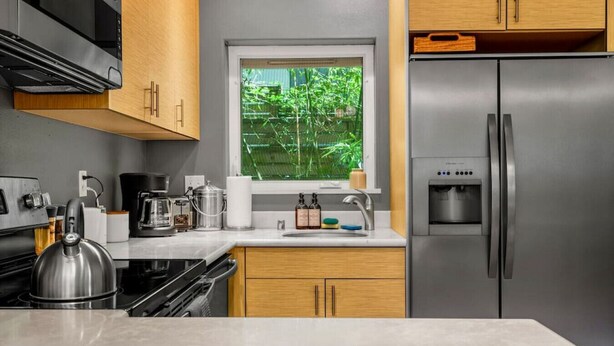 Eine moderne Küche mit einem Edelstahl-Kühlschrank, einem Wasserkocher, einer Kaffeemaschine und einem Fenster mit Blick auf Grünflächen.